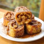 Close-up of Apple Pie French Toast Rollups dusted with cinnamon sugar and drizzled with syrup.