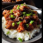 A close-up of delicious Asian Sesame Air Fryer Chicken served over white rice, garnished with sesame seeds and green onions.