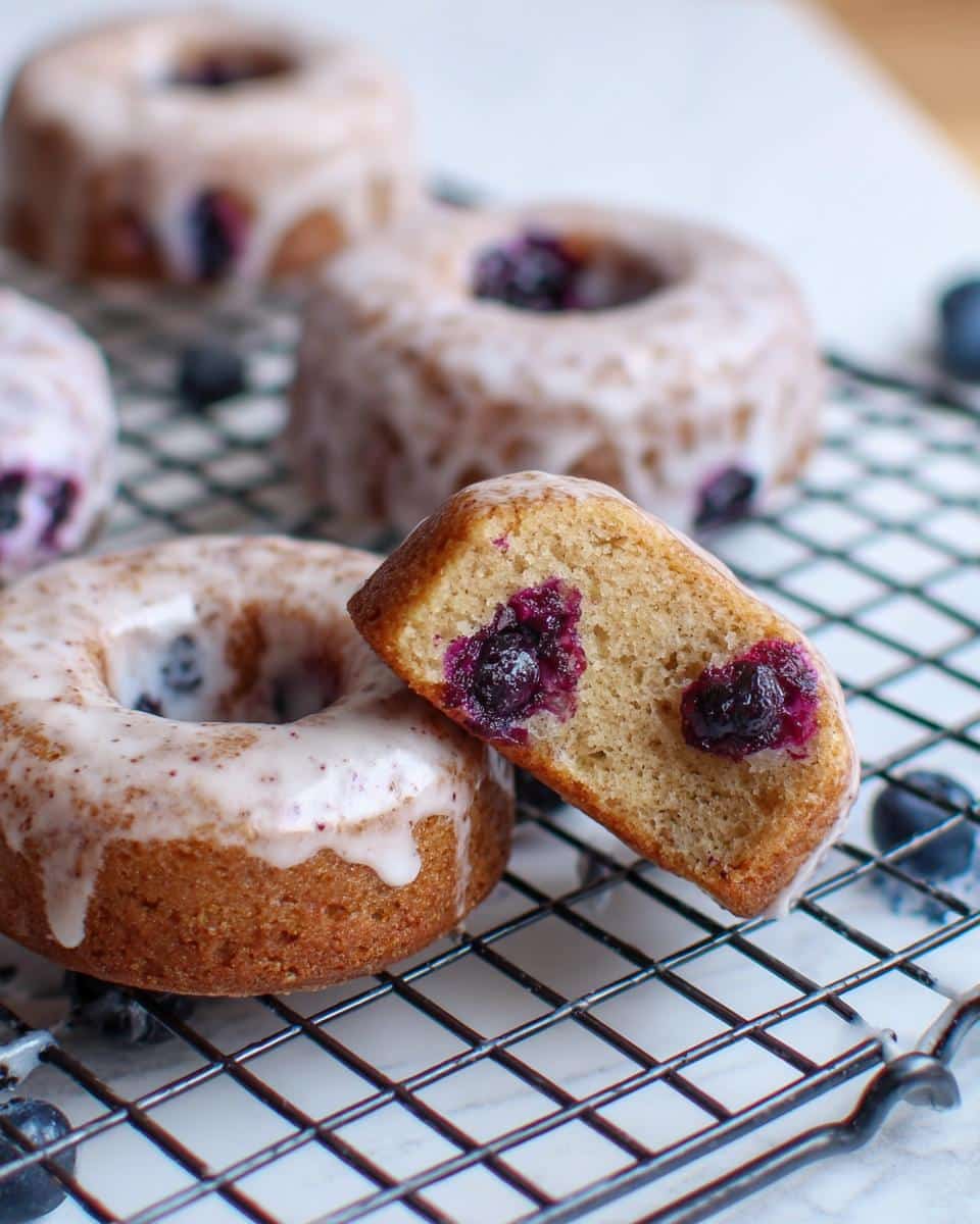 Close-up of a Banana Blueberry Donut cut in half showing moist interior and blueberries, resting on a cooling rack.