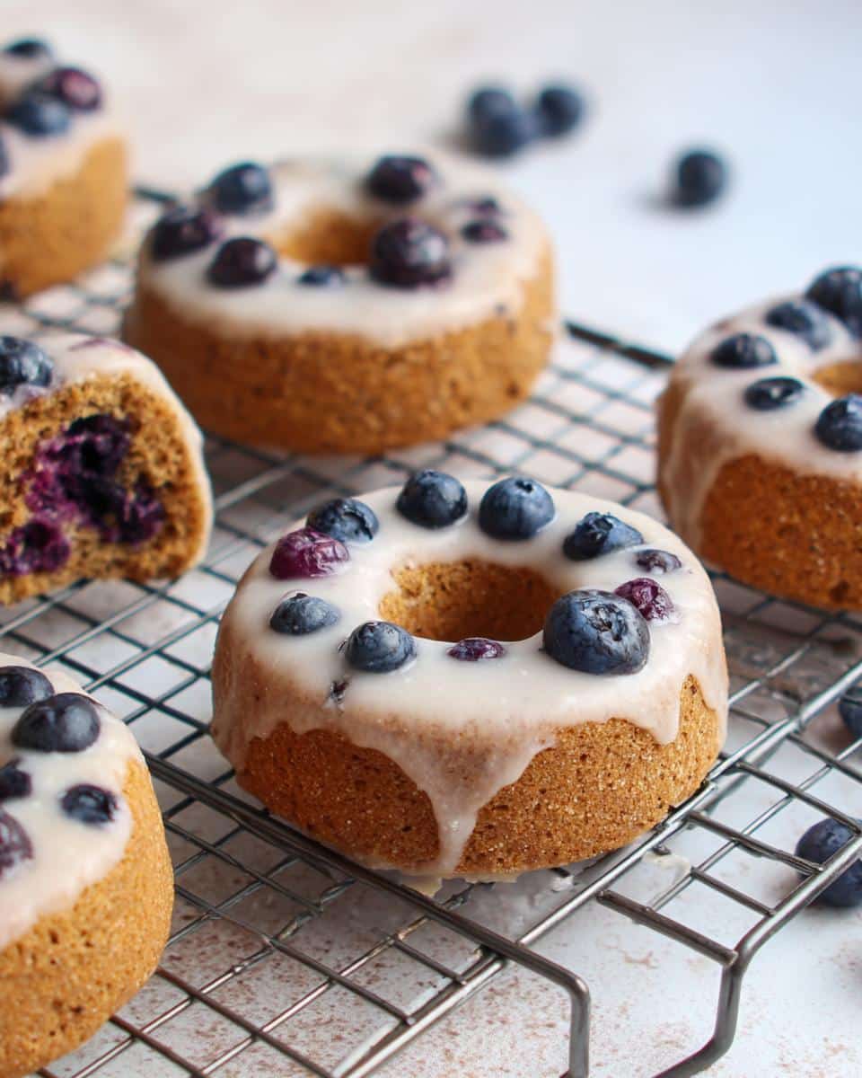 Close-up of a baked Banana Blueberry Donut topped with white glaze and fresh blueberries, cooling on a wire rack.