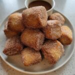 A pile of freshly fried Banana Bread Donut Holes heavily coated in cinnamon sugar on a light plate.