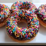 Close-up of several delicious Banana Chocolate Chip Sprinkle Donuts topped with rich chocolate glaze and colorful jimmies.