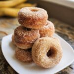 A stack of freshly made Banana Cinnamon Mini Donuts heavily coated in a cinnamon sugar mixture, served on a white plate.