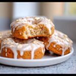 Close-up of stacked Banana Oat Donut Bites with white glaze and scattered rolled oats; one has a bite taken out.