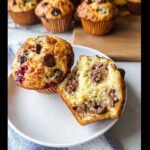 One whole and one halved Banana Pancake Mix Muffins showing a gooey chocolate center on a white plate.