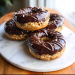 Close-up of four baked Banana Peanut Butter Donuts topped with glossy chocolate glaze and sea salt.