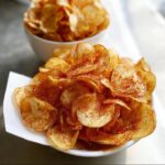 Close-up of a white bowl overflowing with crispy, thinly sliced BBQ Flavored Homemade Chips dusted with red seasoning.