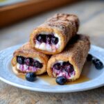 Three stacked Blueberry Cream Cheese French Toast Roll-Ups coated in cinnamon sugar, oozing filling.