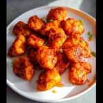 A plate full of delicious Buffalo Air Fryer Chicken Bites, coated in a glossy orange sauce and garnished with green onions.