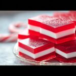 Close-up of layered red and white Candy Cane Jello Shots on a glass plate, dusted with powdered sugar.