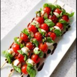 Four skewers of Caprese Skewers with Basil Balsamic Drizzle featuring cherry tomatoes, mozzarella balls, and fresh basil leaves.