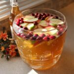 A large glass bowl filled with bubbly Caramel Apple Punch, garnished with sliced apples and cranberries.