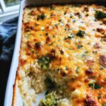 A close-up view of a Cheesy Chicken Broccoli Casserole in a white baking dish, topped with melted golden cheese and parsley.