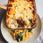 A baked pasta dish with a golden, bubbly cheese crust, served with fusilli pasta and spinach on a plate. This is the Chicken & Cottage Cheese Protein Pasta.