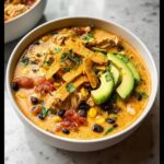 A close-up of a bowl of creamy Chicken Taco Soup, topped with crispy tortilla strips, sliced avocado, and fresh cilantro.