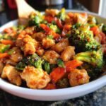 Close-up of a bowl filled with Chinese Chicken Stir Fry, featuring tender chicken pieces, vibrant broccoli florets, and sliced carrots in a glossy sauce.