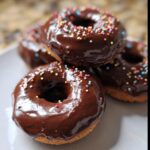 Close-up of several Chocolate-Dipped Banana Donut Holes covered in shiny dark chocolate glaze and rainbow sprinkles.