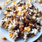 A white bowl filled with a rich Popcorn Snack Mix featuring popcorn, chocolate chunks, nuts, and caramel corn pieces.