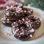 A stack of delicious Chocolate Peppermint Donuts, glazed with dark chocolate and sprinkled with crushed candy canes.