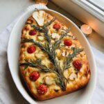 A beautifully decorated Christmas Tree Focaccia Bread topped with rosemary branches, cherry tomatoes, and onions.