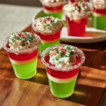 Close-up of festive Christmas Tree Jello Shots with red and green layers, whipped cream, and sprinkles.
