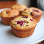 Close-up of a golden-brown Cottage Cheese Protein Muffins topped with bright red baked berries on a white plate.
