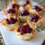 Close-up of flaky phyllo cups filled with brie and topped with glistening cranberry sauce, part of the Cranberry-Brie Phyllo Cups recipe.