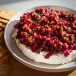 A mound of creamy cheese topped with vibrant Cranberry Jalapeño Dip, served with crackers.