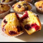 Close-up of a halved Cranberry Orange Muffin, revealing juicy cranberries inside and a sugar-dusted top.
