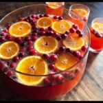 A large glass bowl filled with vibrant Cranberry Orange Punch, garnished with fresh orange slices and whole cranberries.