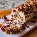 A festive Cranberry Walnut Cheese Log, partially sliced, showing the creamy interior mixed with cranberries and walnuts.