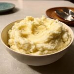 A white bowl filled with fluffy, creamy Christmas mashed potatoes, lightly seasoned with pepper.