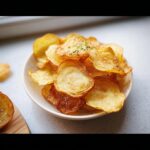 A close-up of a white bowl filled with golden, crispy baked potato chips sprinkled with salt and chives.
