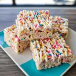 A stack of four Funfetti Marshmallow Popcorn Bars drizzled with white icing and colorful sprinkles.
