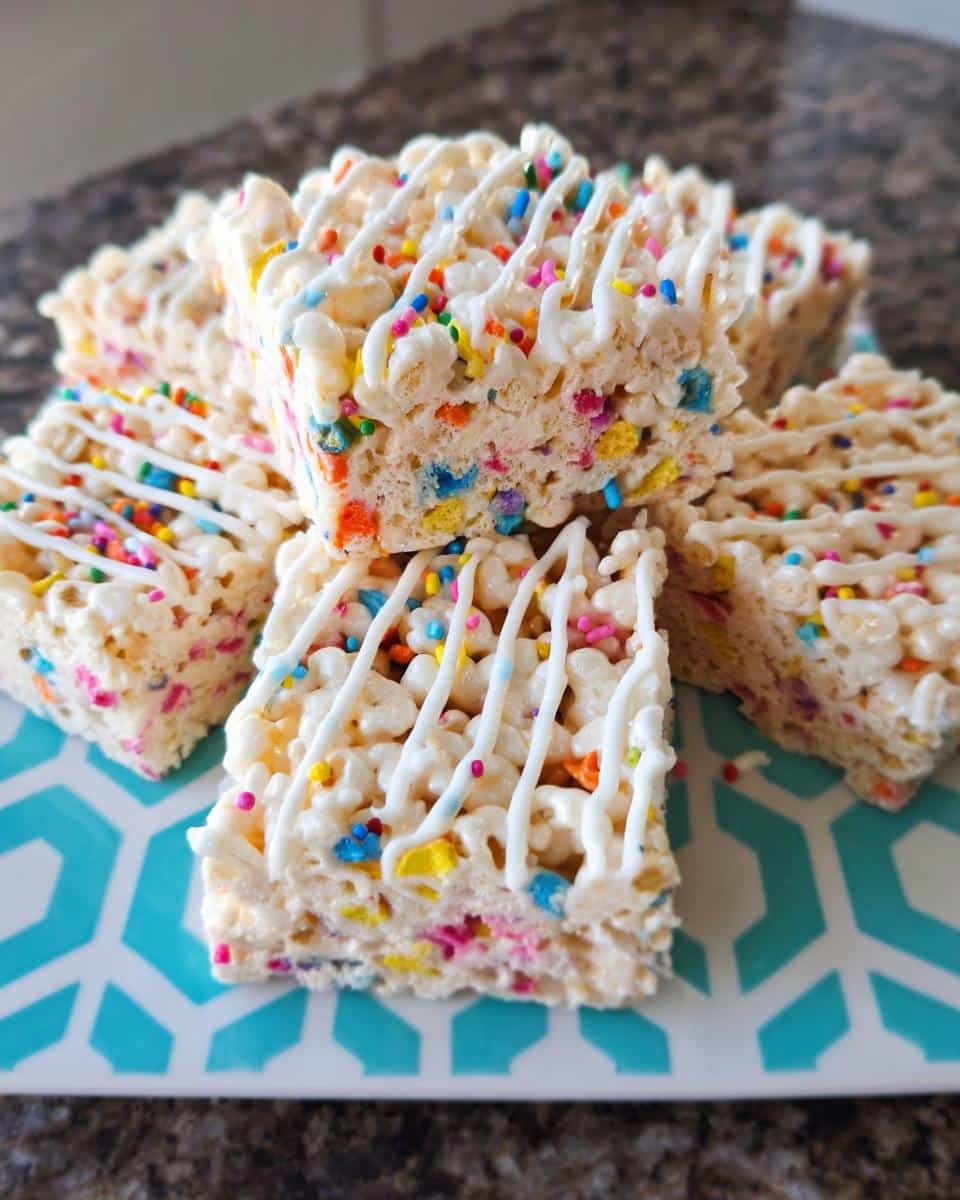 A stack of square Funfetti Marshmallow Popcorn Bars drizzled with white icing and colorful sprinkles.
