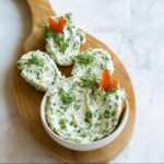 Bowl and slices of bread topped with vibrant Garden Herb Cream Cheese Spread, garnished with dill.