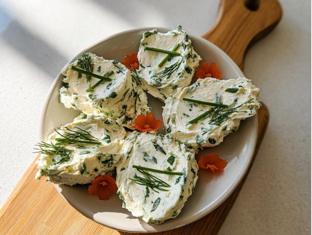 Five dollops of creamy Garden Herb Cream Cheese Spread garnished with fresh dill and chives on a plate.