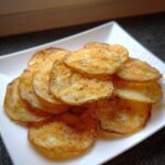 A pile of crispy, golden Garlic Parmesan Potato Chips seasoned with cheese and herbs on a white rectangular plate.