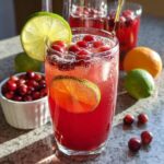 A tall glass filled with vibrant red Ginger Cranberry Punch Mocktail, garnished with lime slices and fresh cranberries.