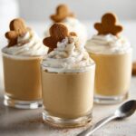 Close-up of Gingerbread Pudding Shots topped with whipped cream and a gingerbread cookie.