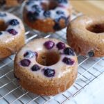 Close-up of a freshly glazed Banana Blueberry Donut topped with whole blueberries resting on a wire cooling rack.