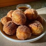 A pile of warm Gluten-Free Banana Donut Holes coated in cinnamon sugar, served with a side of caramel dip.