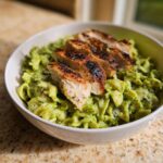 Close-up of High Protein Pesto Pasta Bowls topped with perfectly grilled, sliced chicken breast.
