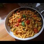 A skillet filled with creamy High Protein Tomato Basil Pasta, zucchini slices, and roasted cherry tomatoes.