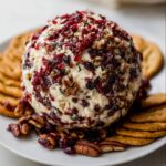 A festive Holiday Cheese Ball with Cranberries & Pecans, coated in dried fruit and nuts, served with crackers.
