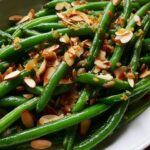 Close-up of bright green beans tossed with toasted sliced almonds and brown butter/sugar topping for Holiday Green Bean Almondine.