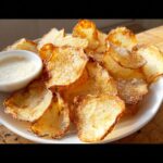 A plate piled high with golden, crispy Homemade Air Fryer Potato Chips sprinkled with salt, served with a small bowl of creamy dip.