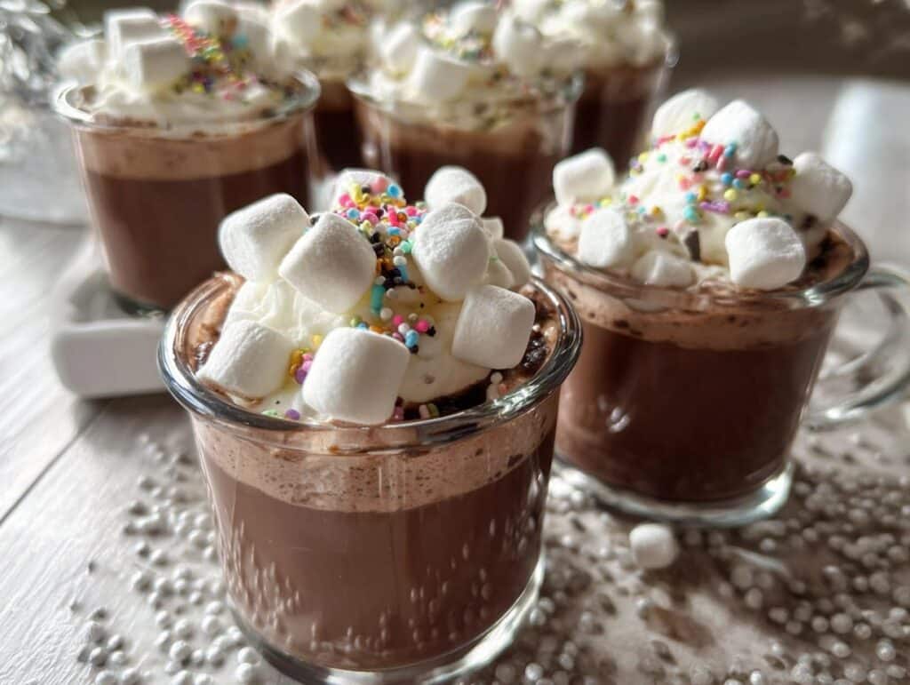 Close-up of creamy Hot Chocolate Jello Shots topped with whipped cream, mini marshmallows, and colorful sprinkles.