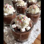 Close-up of creamy Hot Chocolate Jello Shots topped with whipped cream, marshmallows, and colorful sprinkles.