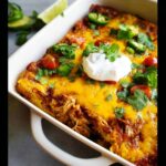 A close-up of a Keto Chicken Enchilada Casserole topped with melted cheese, sour cream, cilantro, tomatoes, and jalapeños.
